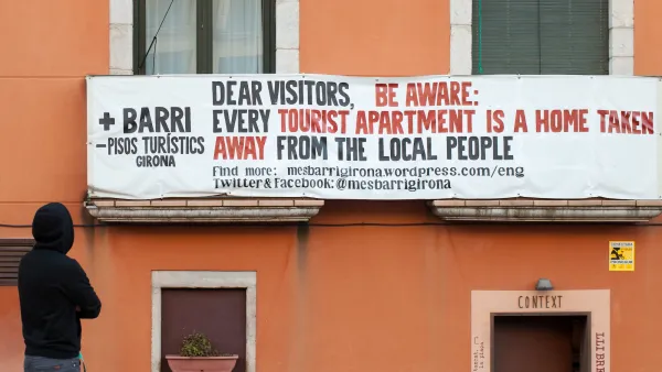 Sign saying “Dear visitors, be aware: every tourist apartment is a home taken away from the local people” hung on orange building in Girona, Spain.