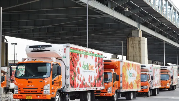 Row of refrigerated trucks with food delivery company logos under freeway overpass in the Bronx, NYC.