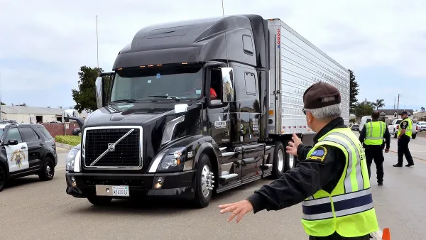 Black 18-wheeler truck being stopped by inspectors in black jackets and yellow safety vests.