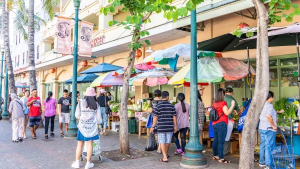 People walk down street with colorful umbrellas in front of ground floor retail in Honolulu, Hawaii.