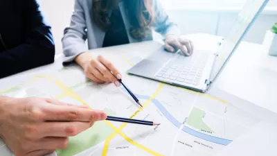 Close-up of two people pointing at a printed city map with pencils with a laptop in the background