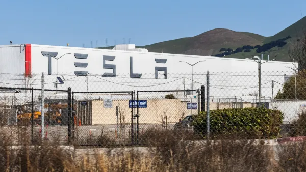 Tesla factory building in Fremont, California visible behind chain link fence.