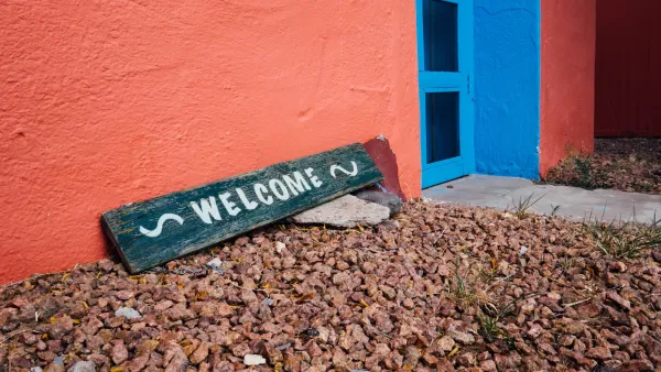 Green "welcome" sign leaning on wall of orange home with gravel ground in US Southwest.