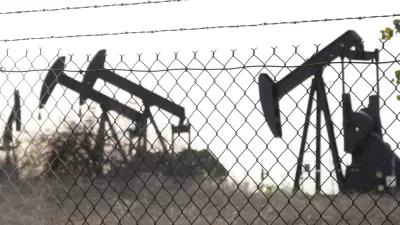 View of black oil wells behind chain link fence with barbed wire top