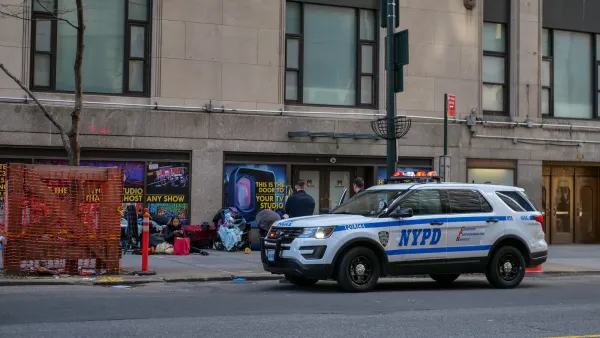 White NYPD SUV parked curbside next to unhoused people sitting on sidewalk.
