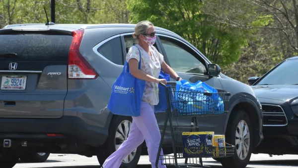 Woman pushing blue shopping cart in parking lot next to grey Honda SUV.