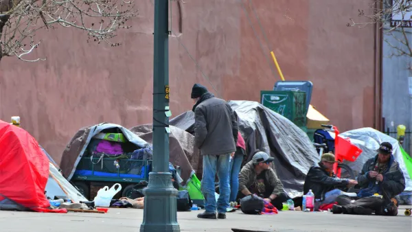 Unhoused people and tents surrounded by everyday items on sidewalk in Denver, Colorado.