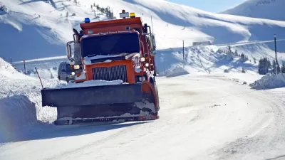 Orange snowplow clearing snow on Colorado road