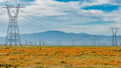 Power transmission lines surrounded by orange California poppies and silhouette of mountains in background