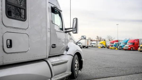 White big rig truck parked in lot with other colorful trucks visible in background.