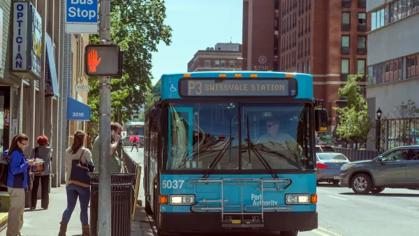 Blue Pittsburgh punlic transit bus with people boarding at sidewalk bus stop.