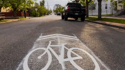 Street-level view of sharrow symbol on asphalt with parked car in background