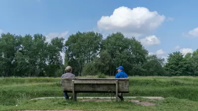 Two friends sit and talk at a social distance in Fletcher Moss park, Manchester, UK