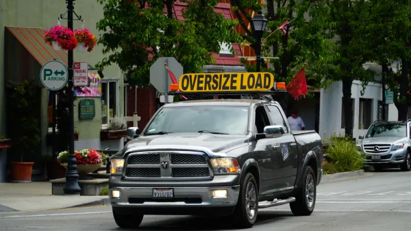 Pick-up truck on small town street with yellow "Oversize Load" sign 