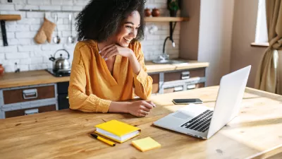 Woman in yellow top sitting at wood kitchen island looking at laptop