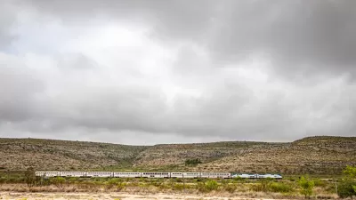 Amtrak Sunset Limited train viewed from the side passing low desert hills in West Texas