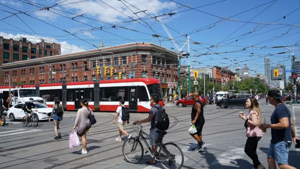 Red streetcar on busy street intersection with public transit wires overhead in Toronto, Canada.