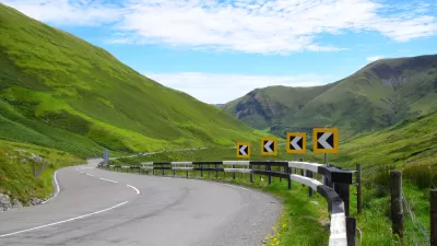 Asphalt road with yellow and black turn warning signs winding through green Welsh mountain landscape