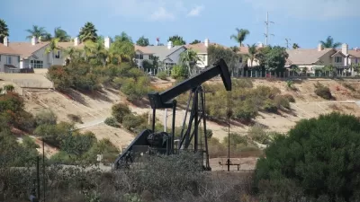 Black pumpjack oil derrick with houses in background