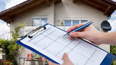Person holding clipboard with checklist and pen with blurred house in the background