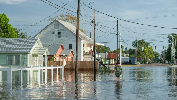 Two people walk through flooded street with wood homes in Louisiana.