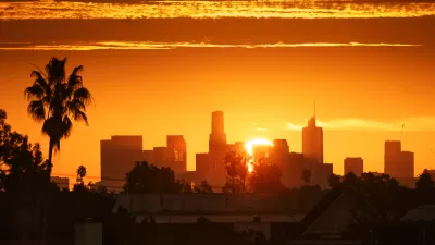 View of Los Angeles skyline against a bright orange sky with a palm tree at left