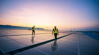 Solar panels on a rooftop with two workers in hard hats and safety vests walking between panels