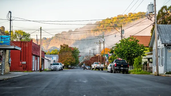 Colorful wood buildings line wide asphalt street in West Virginia small town with misty hills in background.