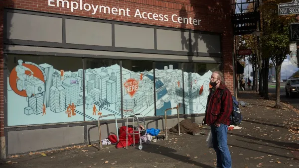 Man wearing red and black plaid shirt stands in front of employment center office in the ground floor of urban office building.