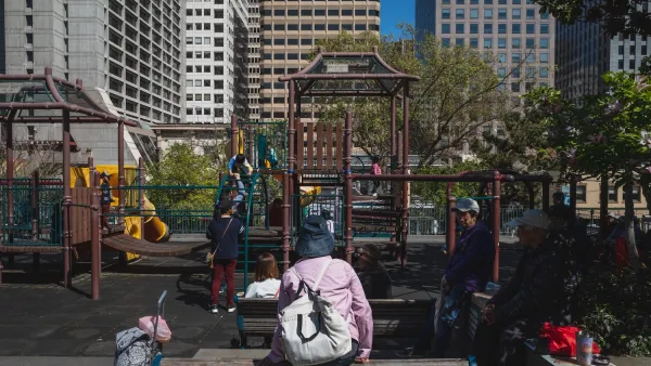 Adults watching over children playing on urban playground in Chinatown, San Francisco with high-rises in background.