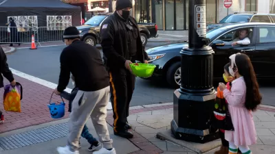 Children in Halloween costumes at a crosswalk with officer offering bowl of candy