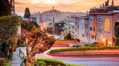 View of downtown San Francisco from top of windy street at sunset with Coit Tower in distance