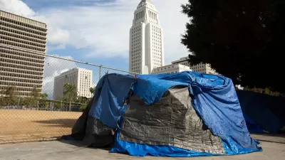 A tent covered in blue and black tarps sits on a downtown Los Angeles sidewalk with the white ziggurat-topped L.A. City Hall looming in the background