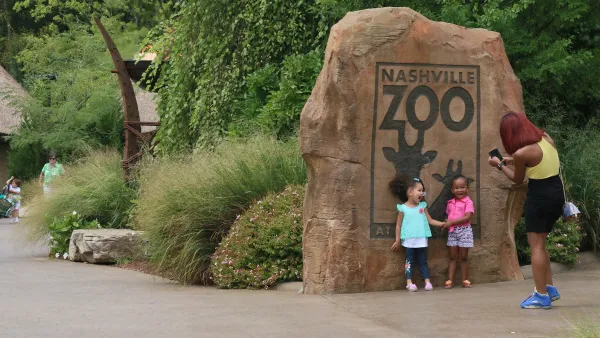 Two young children stand in front of Nashville Zoo logo on large rock as mother takes their photo.