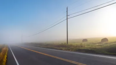 Foggy rural road with power lines and haystacks along the side