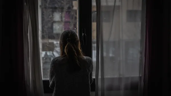 Woman stands in front of window looking out at rain in a dark room.