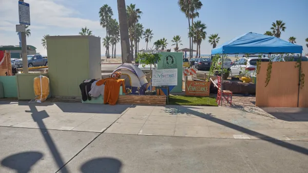 Tents used by unhoused people on concrete walkway with Venice Beach, California beach and palm trees in background.