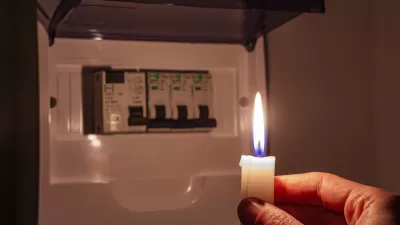 Hand holding candle toward small electrical fuse box in the dark