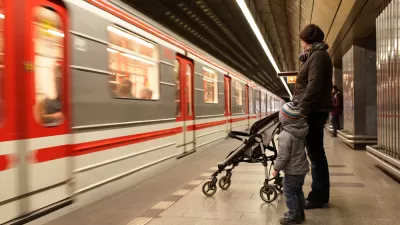 Woman with child and stroller waiting on Prague subway platform with blurred train passing by.