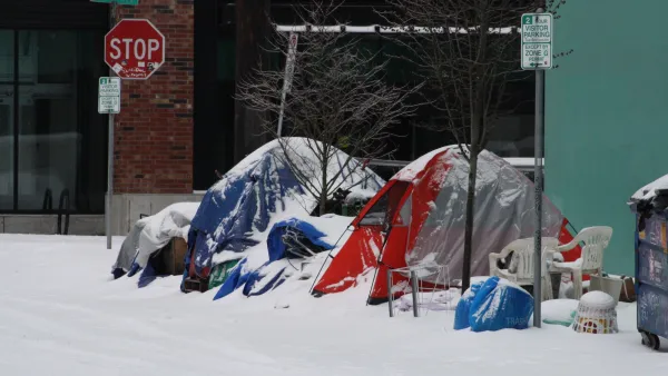 Tents set up by unhoused people surrounded by assorted everyday items on snowy Portland sidewalk.