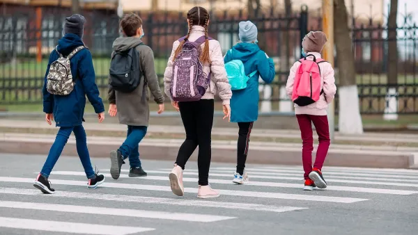Group of children with backpacks walking across a street at a crosswalk.