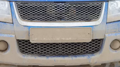 Close-up of license plate on blue car covered in mud, license plate is unreadable.
