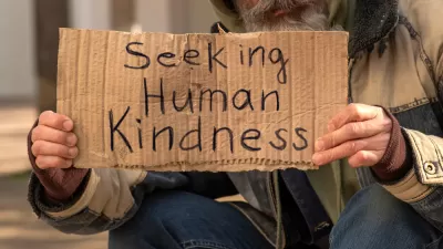 Unhoused man holding sign that reads "Seeking human kindness"