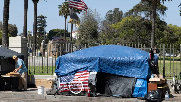 Tent set up on sidewalk covered with blue tarp and American flag on front next to fence to VA campus in West Los Angeles, California.