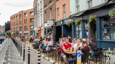 People sitting at outdoor dining tables next to bike lane protected by delineators and three-story buildings in Dublin, Ireland