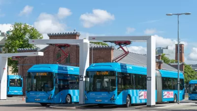 Blue electric transit buses at a charging bay in Gothenburg, Sweden with two-story red brick building in background