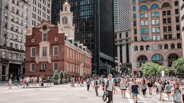 Old State House in Boston, MA b uilt in 1713 with busy crosswalk in front of it surrounded by mode modern buildings.