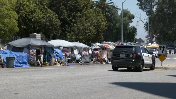 LAPD SUV drives past homeless encampment lined up along street curb in Los Angeles, California.