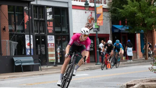 Cyclist in pink jersey and white helmet riding a bike in front of group of several other cyclists in Fayetteville, Arkansas.