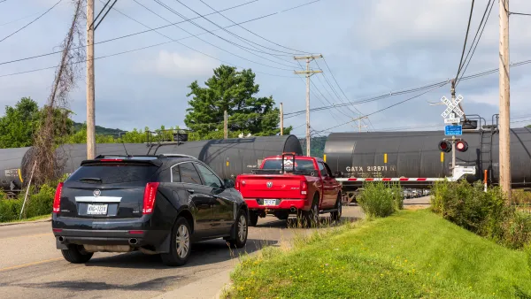 Cars waiting on the road as a train passes a railroad crossing.